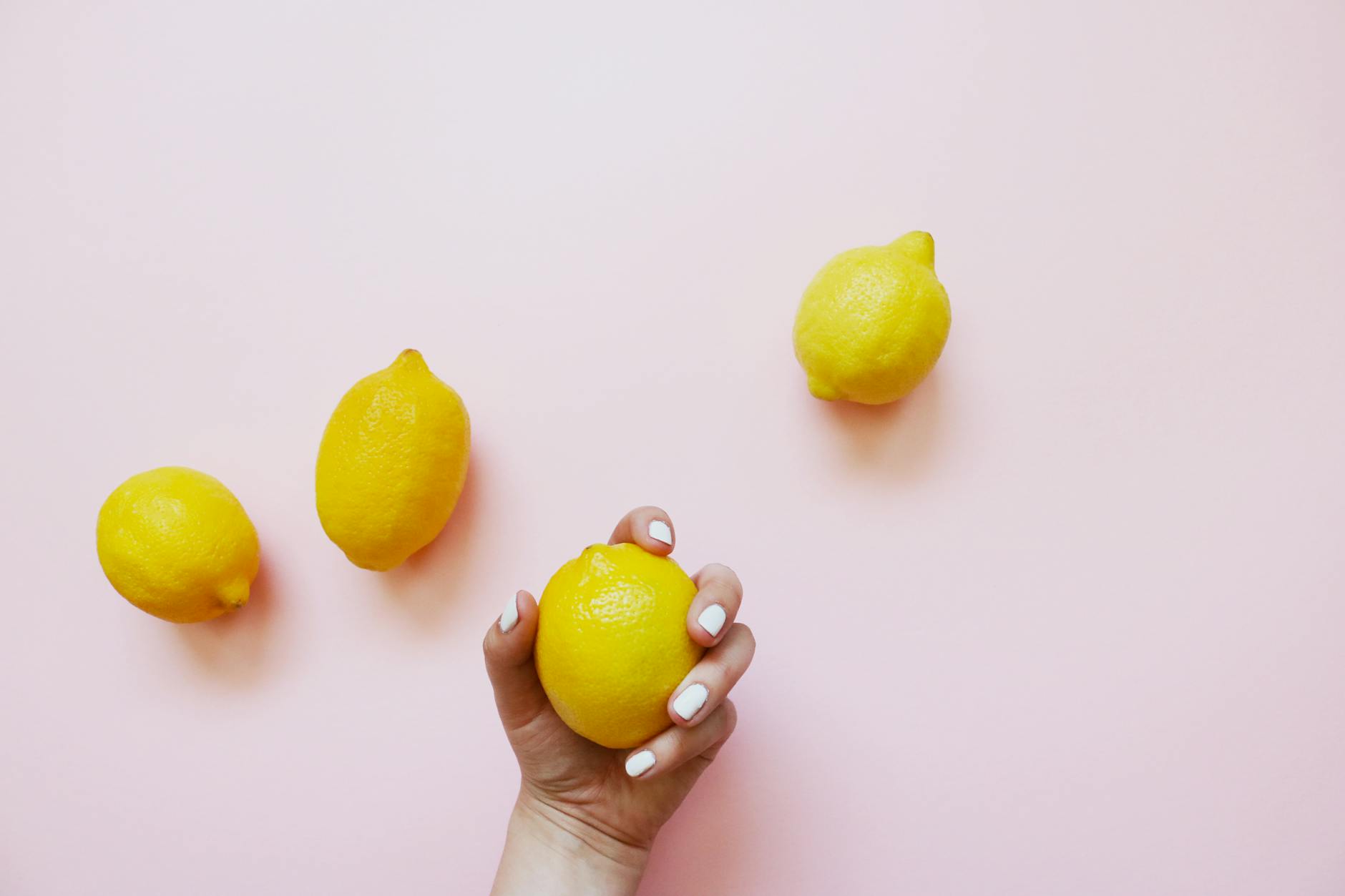 A hand holding a lemon on a soft pink background, symbolizing gentle sensation and pleasure recovery