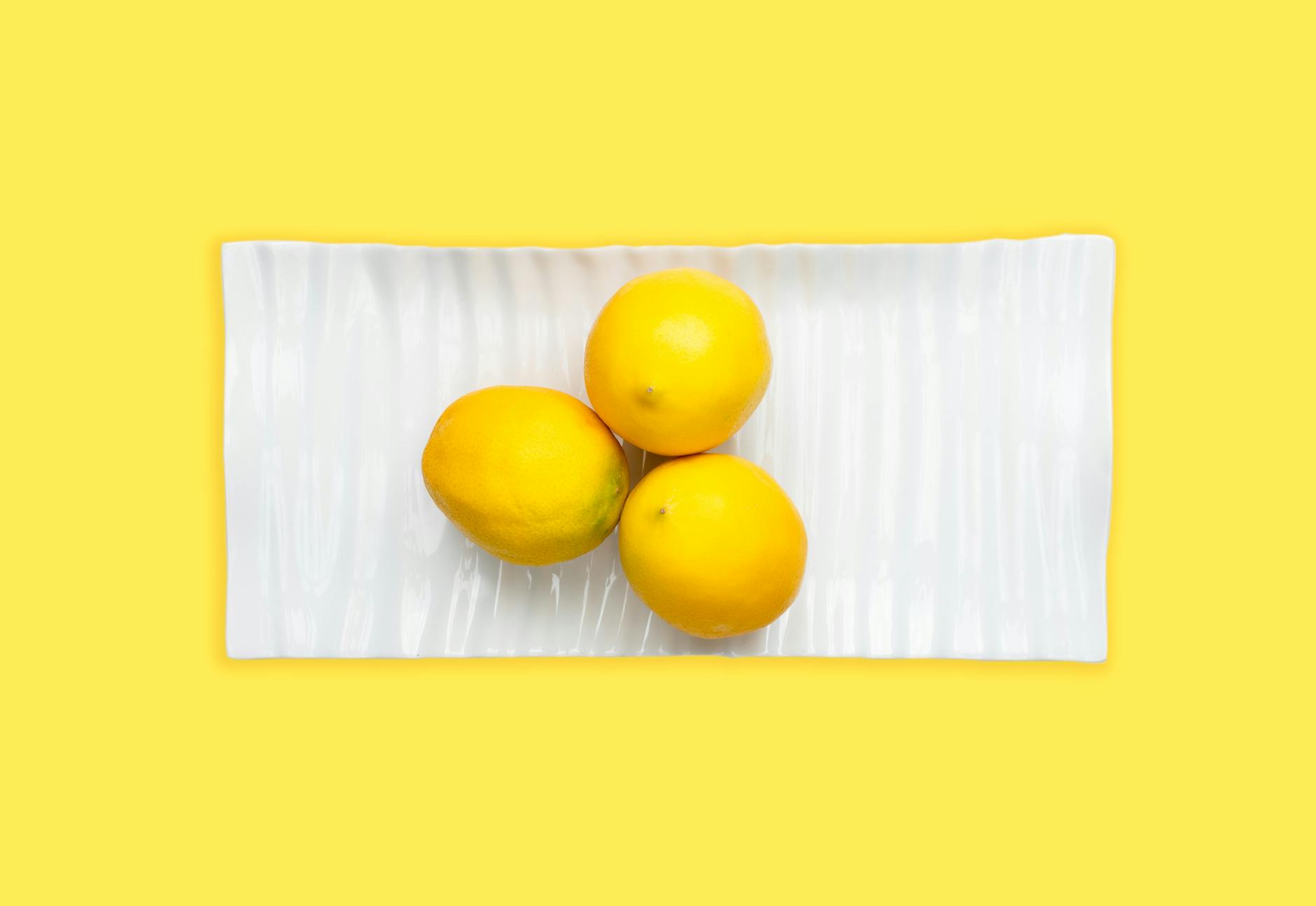 Fresh lemons on white plate against yellow background, symbolizing bright, vibrant approaches to renewed pleasure
