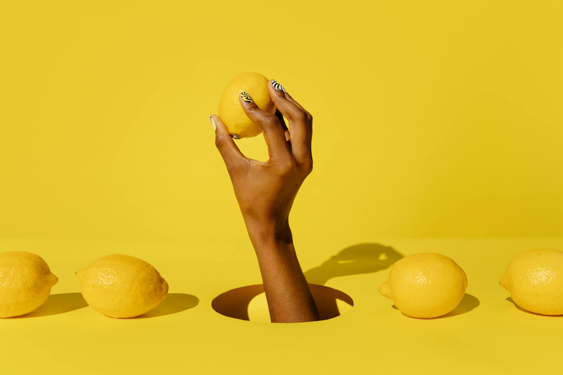 A hand holding a fresh lemon against a bright yellow background, symbolizing renewal and a fresh start.