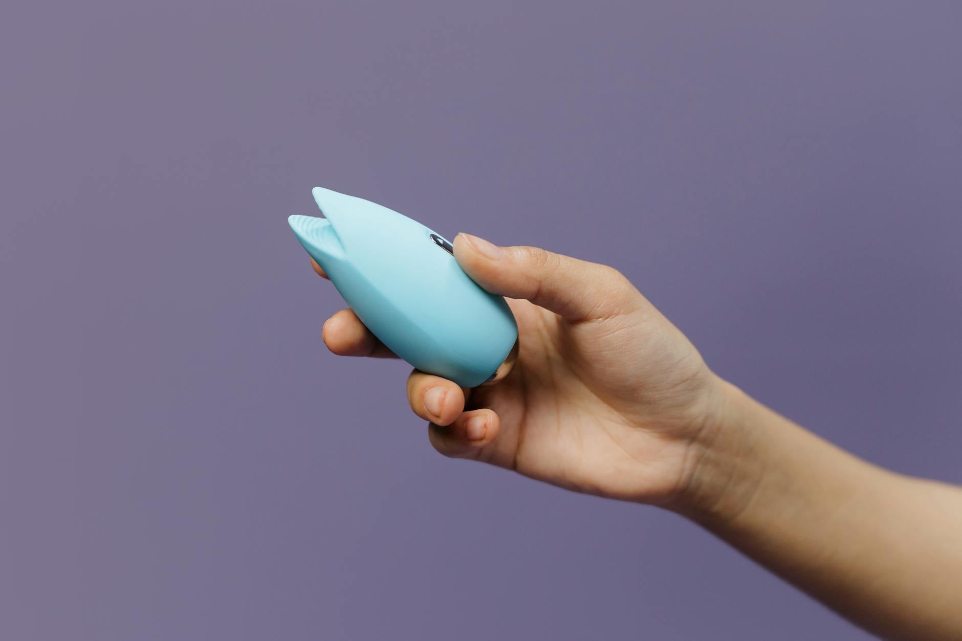 A blue silicone lemon clitoral vibrator held gently in hand against a purple background