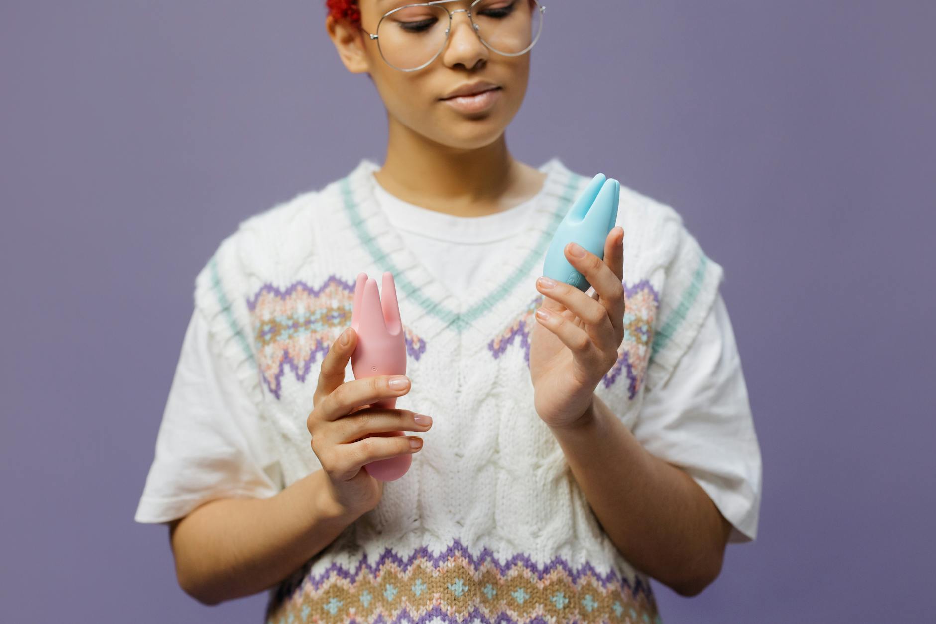 Person holding blue and pink silicone vibrators in contemplation